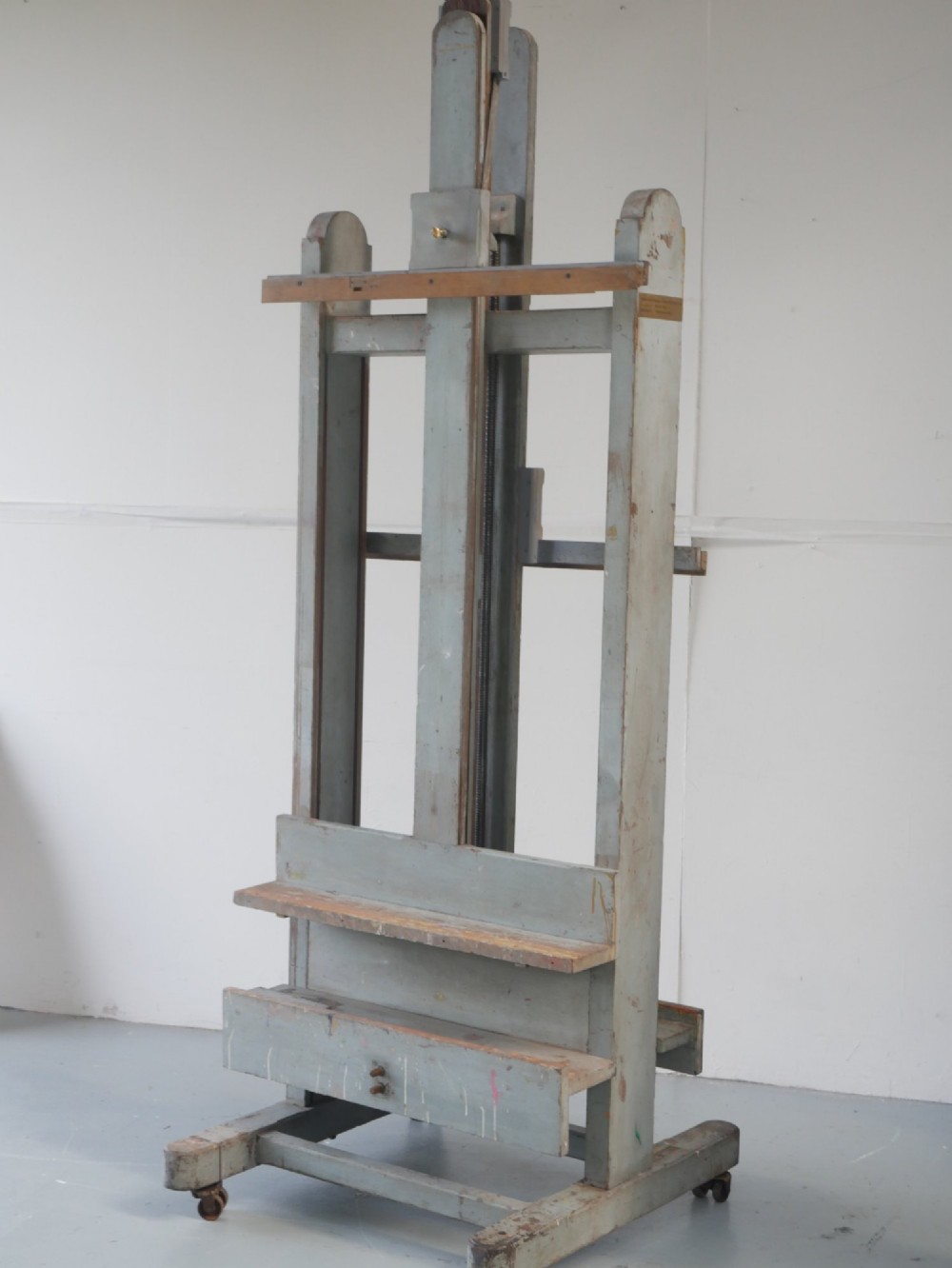 A large floor-standing double-sided timber studio easel with a distressed grey finish, adjustable height mechanism, and metal castor feet. View IV