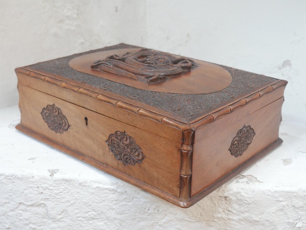 A rectangular Anglo-Indian carved teak box featuring a raised central motif on the lid, carved bamboo-style border trim, and side decorative panels.