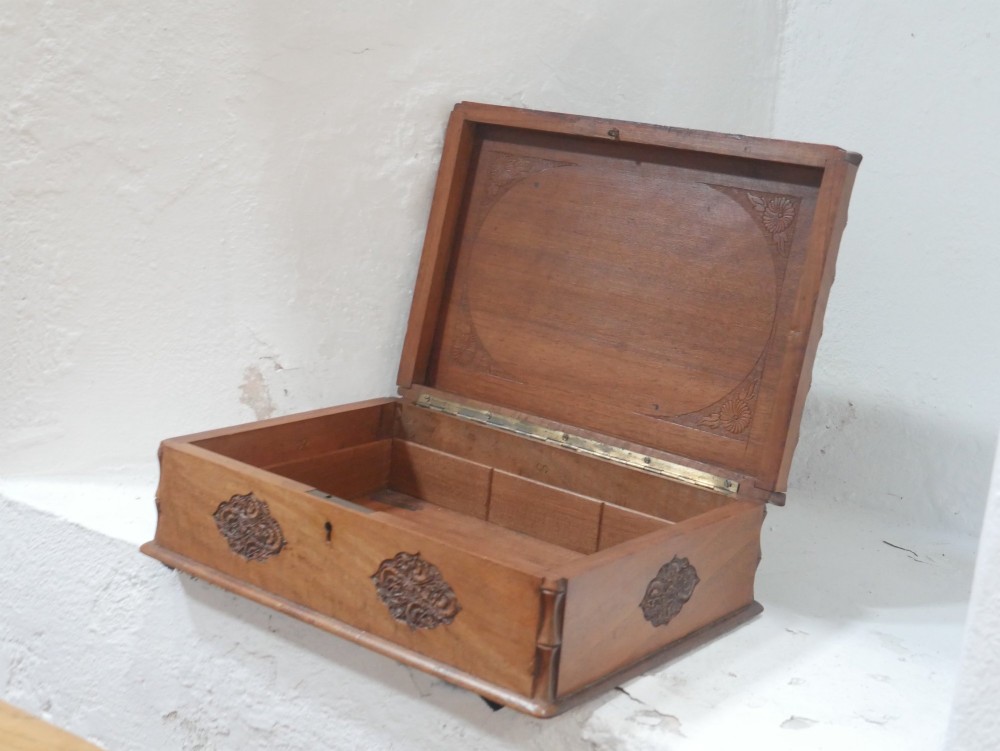 A rectangular Anglo-Indian carved teak box featuring a raised central motif on the lid, carved bamboo-style border trim, and side decorative panels. View II