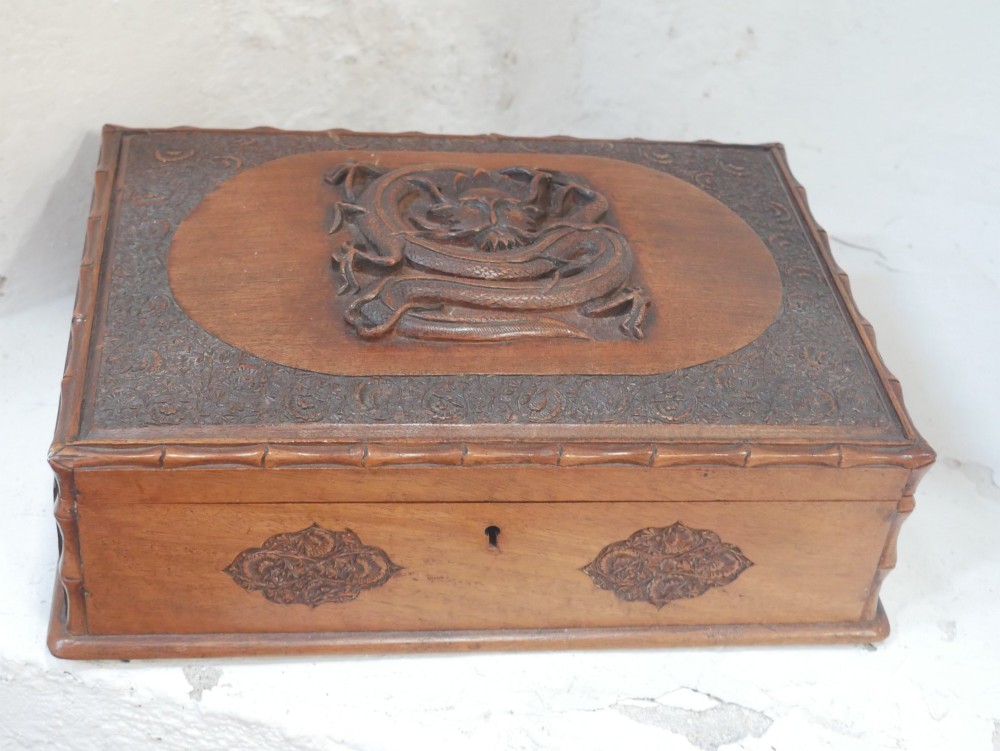 A rectangular Anglo-Indian carved teak box featuring a raised central motif on the lid, carved bamboo-style border trim, and side decorative panels. View V
