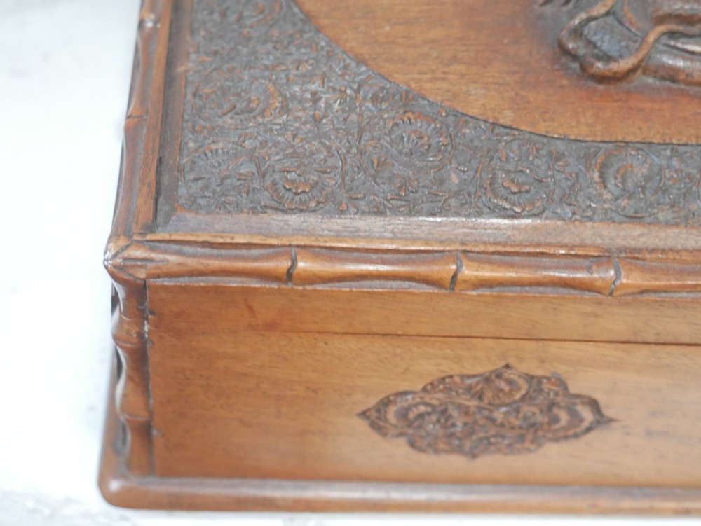 A rectangular Anglo-Indian carved teak box featuring a raised central motif on the lid, carved bamboo-style border trim, and side decorative panels. View VII