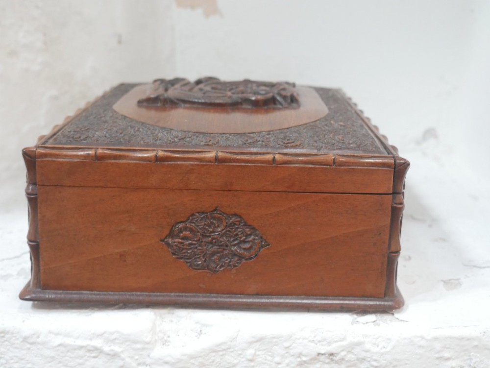 A rectangular Anglo-Indian carved teak box featuring a raised central motif on the lid, carved bamboo-style border trim, and side decorative panels. View IX
