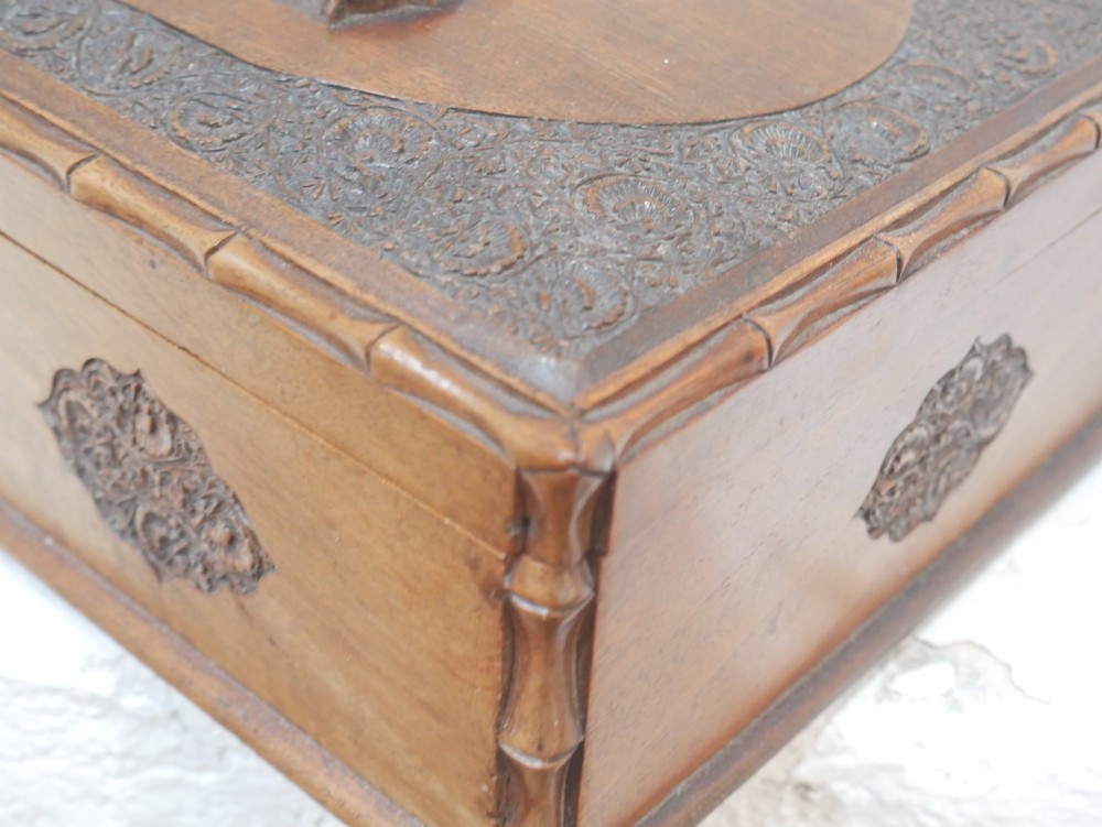 A rectangular Anglo-Indian carved teak box featuring a raised central motif on the lid, carved bamboo-style border trim, and side decorative panels. View X