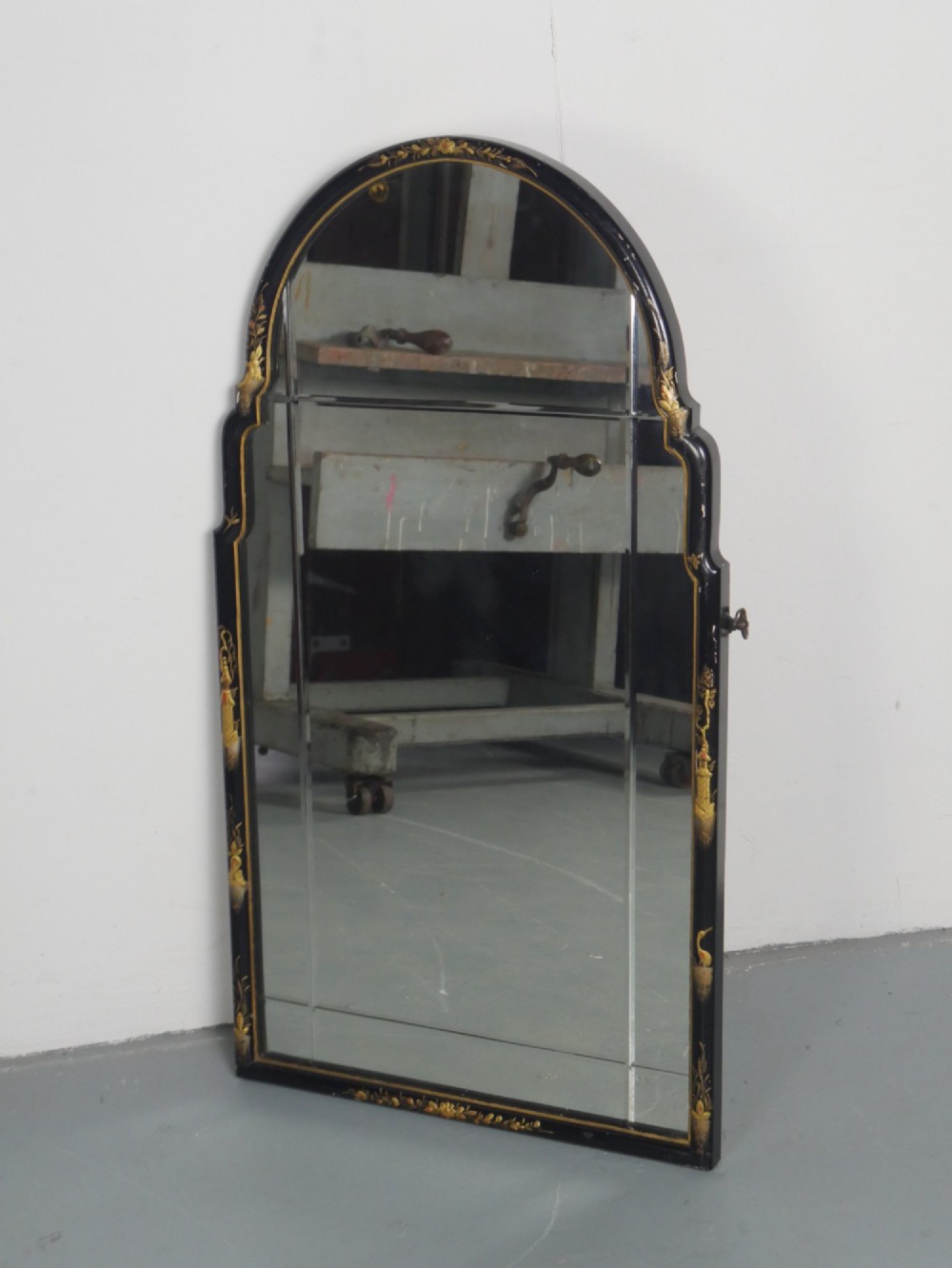 An arched black lacquer wall mirror decorated with gold hand-painted chinoiserie details and sectioned bevelled glass.