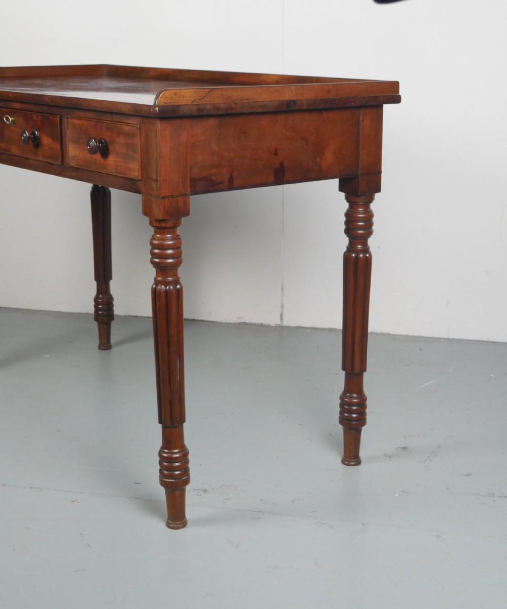 A Regency period mahogany writing table featuring three drawers with wooden knobs, a three-sided gallery rim, and four reeded legs. View III