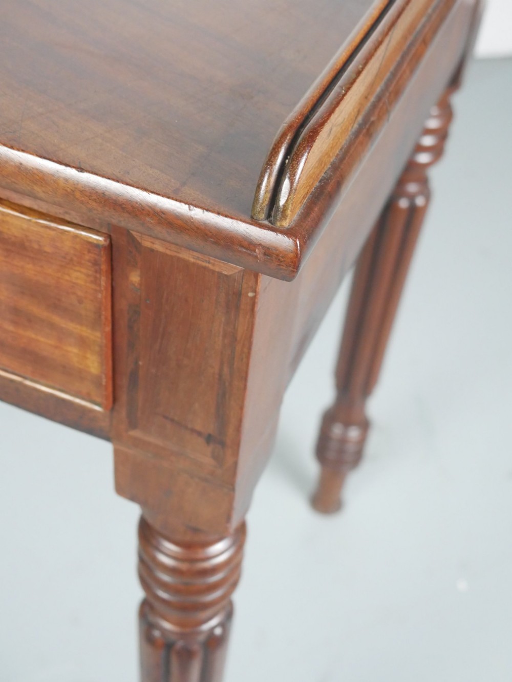 A Regency period mahogany writing table featuring three drawers with wooden knobs, a three-sided gallery rim, and four reeded legs. View V