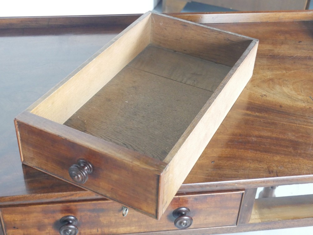 A Regency period mahogany writing table featuring three drawers with wooden knobs, a three-sided gallery rim, and four reeded legs. View IX