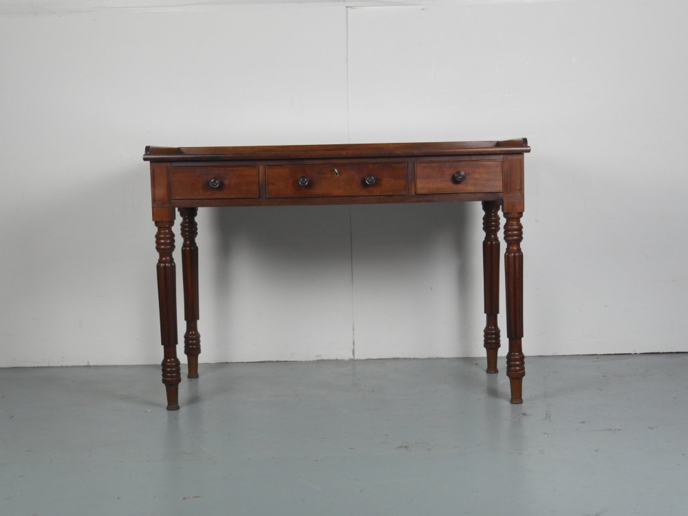 A Regency period mahogany writing table featuring three drawers with wooden knobs, a three-sided gallery rim, and four reeded legs. View XIII