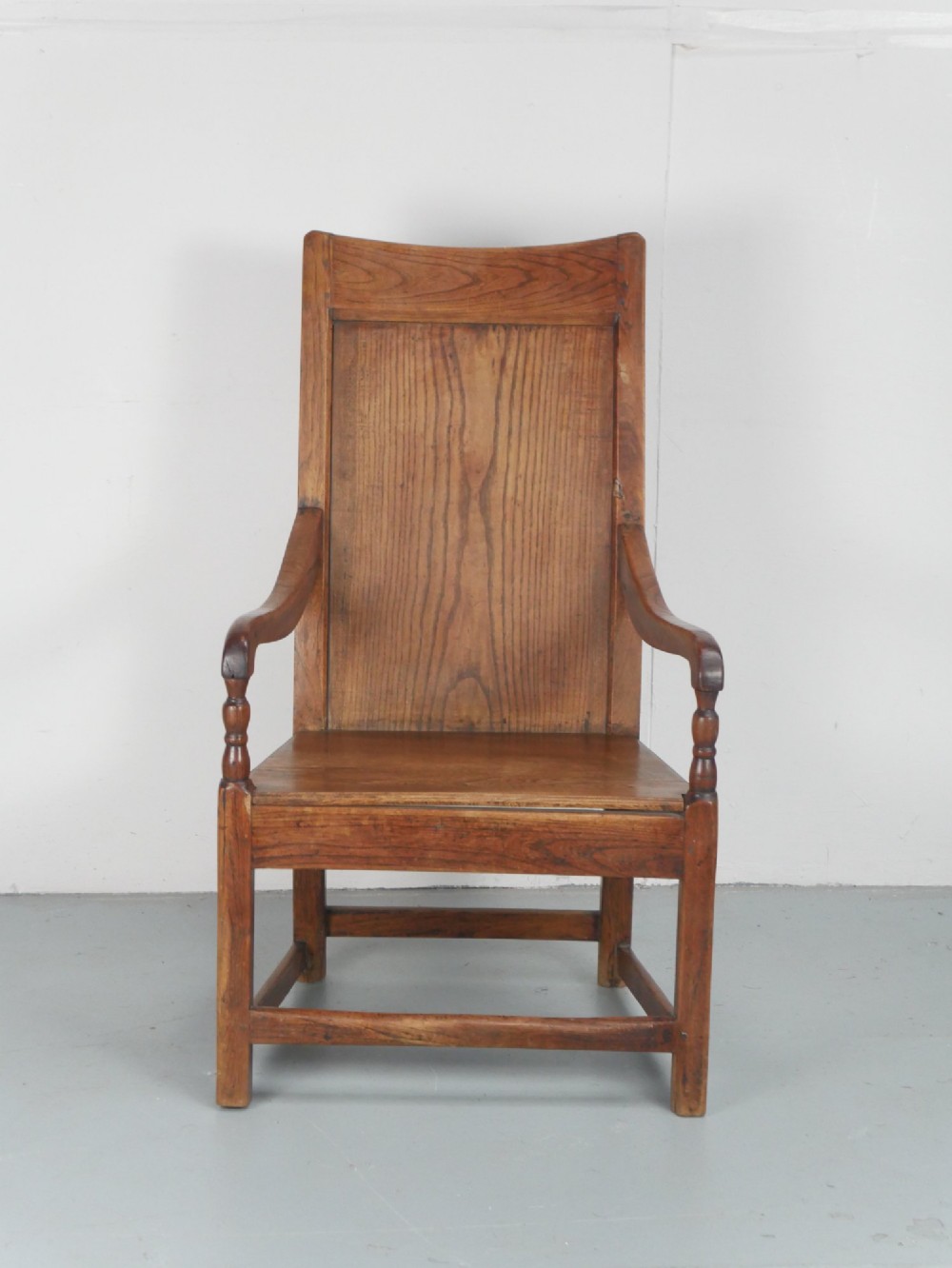 An early 19th-century country oak armchair featuring a high panelled backrest, curved arms, turned front supports, and a square stretcher base. View II