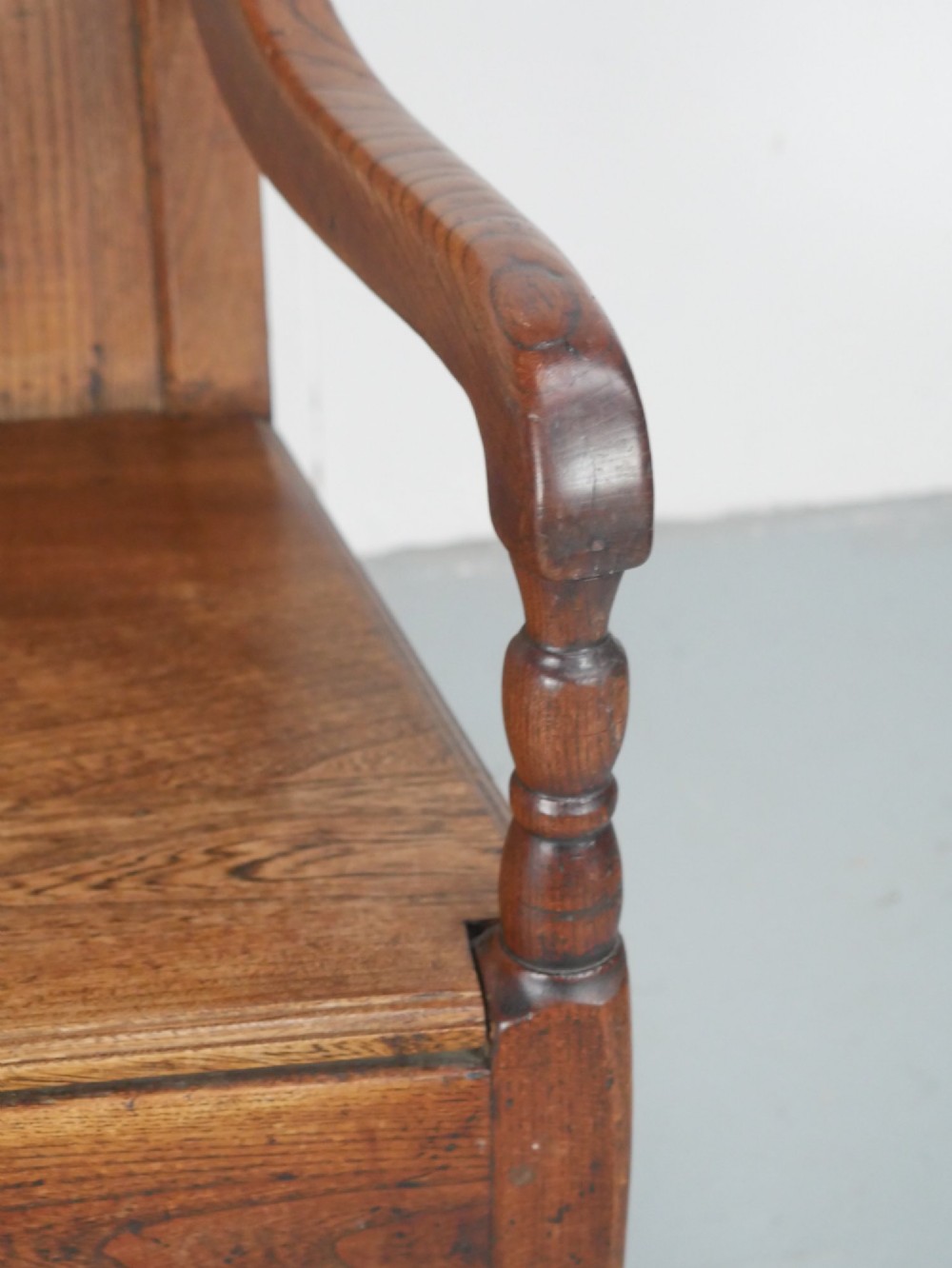 An early 19th-century country oak armchair featuring a high panelled backrest, curved arms, turned front supports, and a square stretcher base. View III