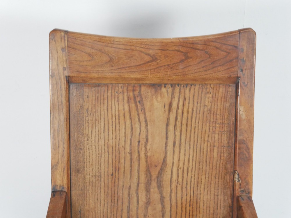 An early 19th-century country oak armchair featuring a high panelled backrest, curved arms, turned front supports, and a square stretcher base. View V