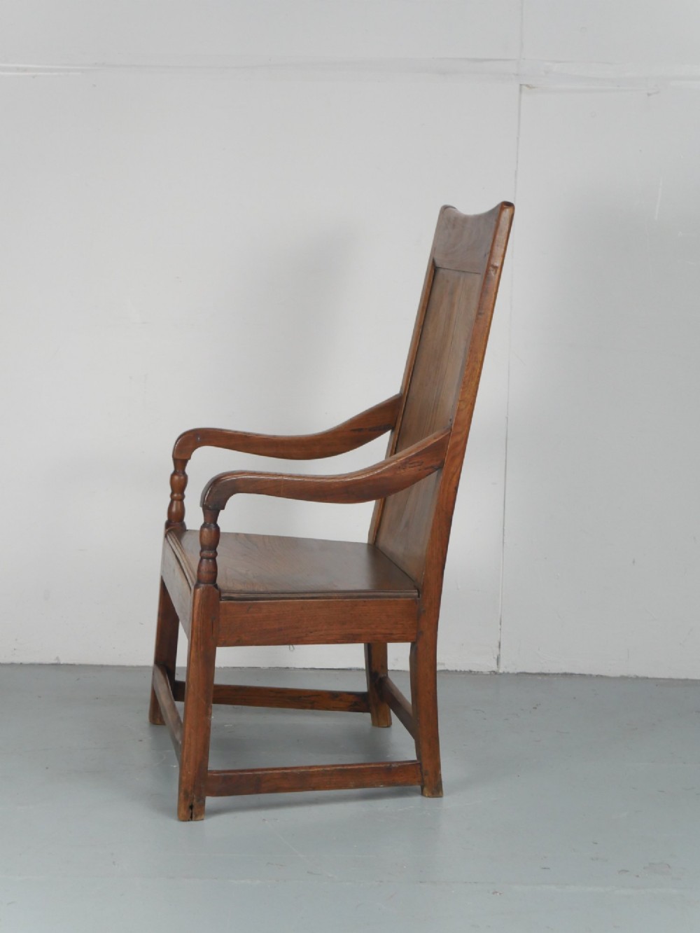 An early 19th-century country oak armchair featuring a high panelled backrest, curved arms, turned front supports, and a square stretcher base. View VI