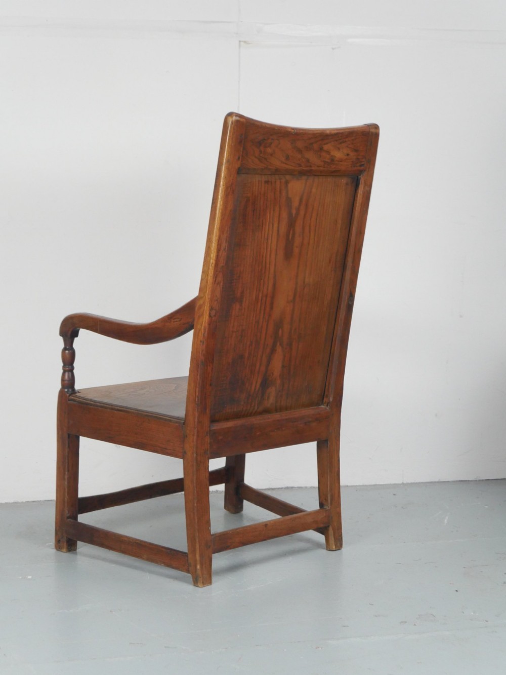 An early 19th-century country oak armchair featuring a high panelled backrest, curved arms, turned front supports, and a square stretcher base. View VII