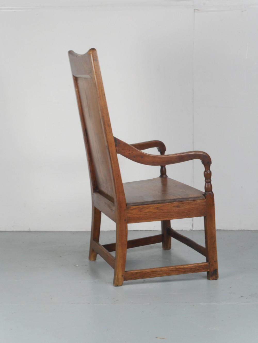 An early 19th-century country oak armchair featuring a high panelled backrest, curved arms, turned front supports, and a square stretcher base. View VIII