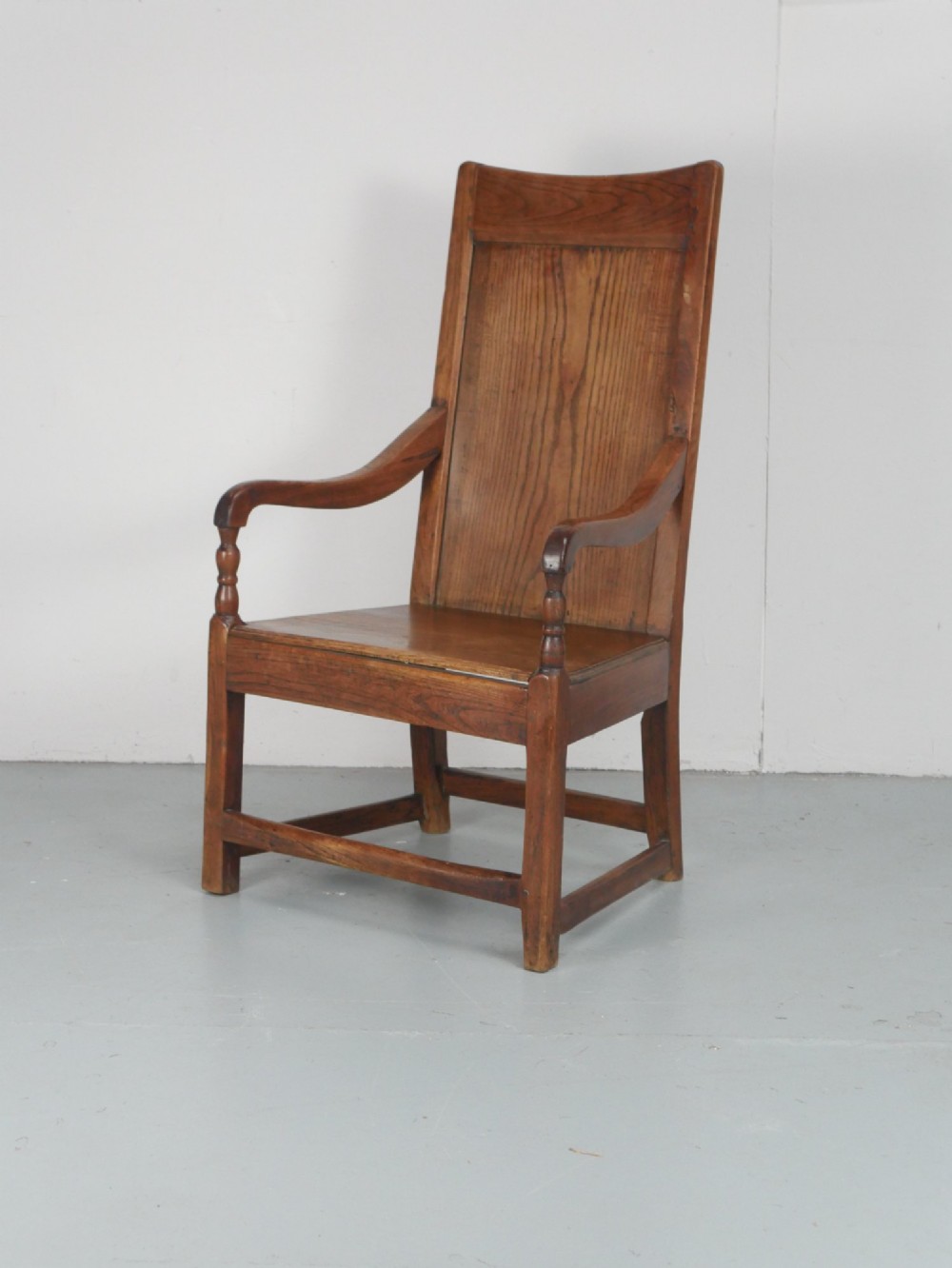 An early 19th-century country oak armchair featuring a high panelled backrest, curved arms, turned front supports, and a square stretcher base. View XI