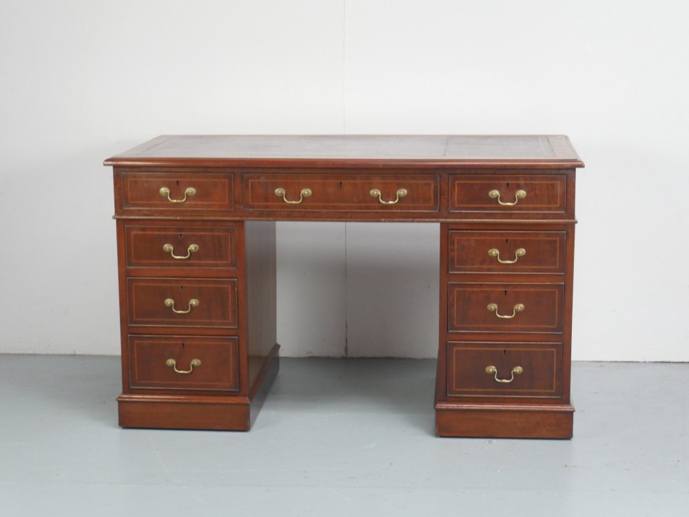 An Edwardian mahogany kneehole pedestal desk featuring an inset writing top, inlaid drawer borders, and nine drawers fitted with brass swan-neck handles.