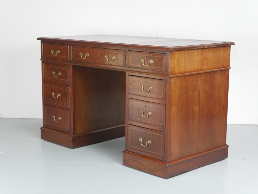 An Edwardian mahogany kneehole pedestal desk featuring an inset writing top, inlaid drawer borders, and nine drawers fitted with brass swan-neck handles. View II