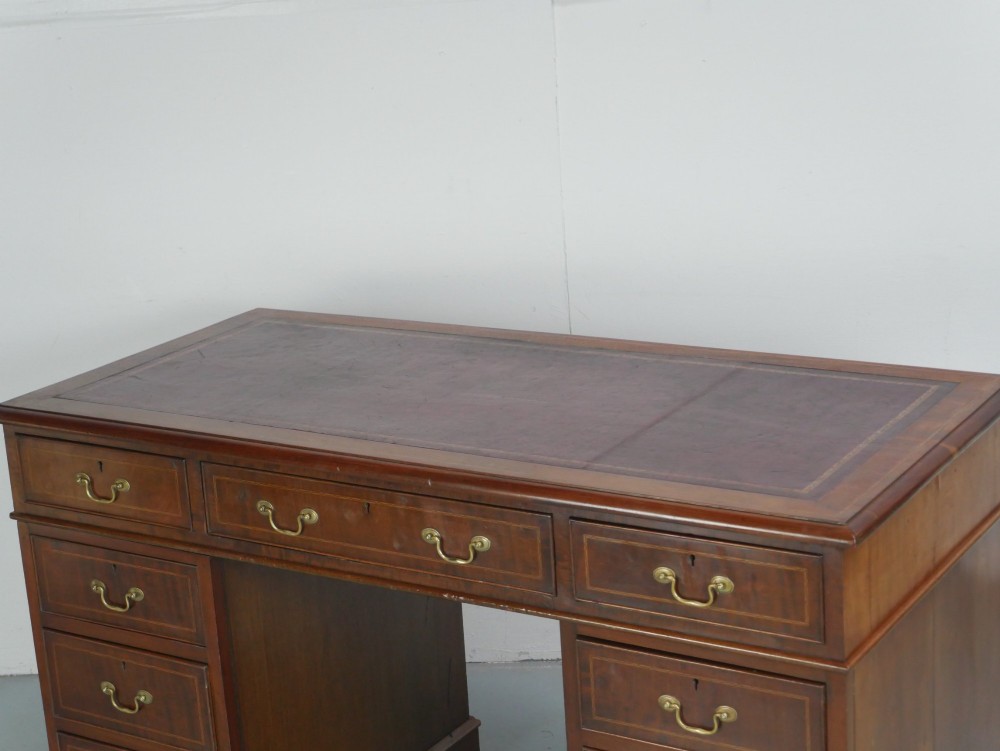 An Edwardian mahogany kneehole pedestal desk featuring an inset writing top, inlaid drawer borders, and nine drawers fitted with brass swan-neck handles. View III