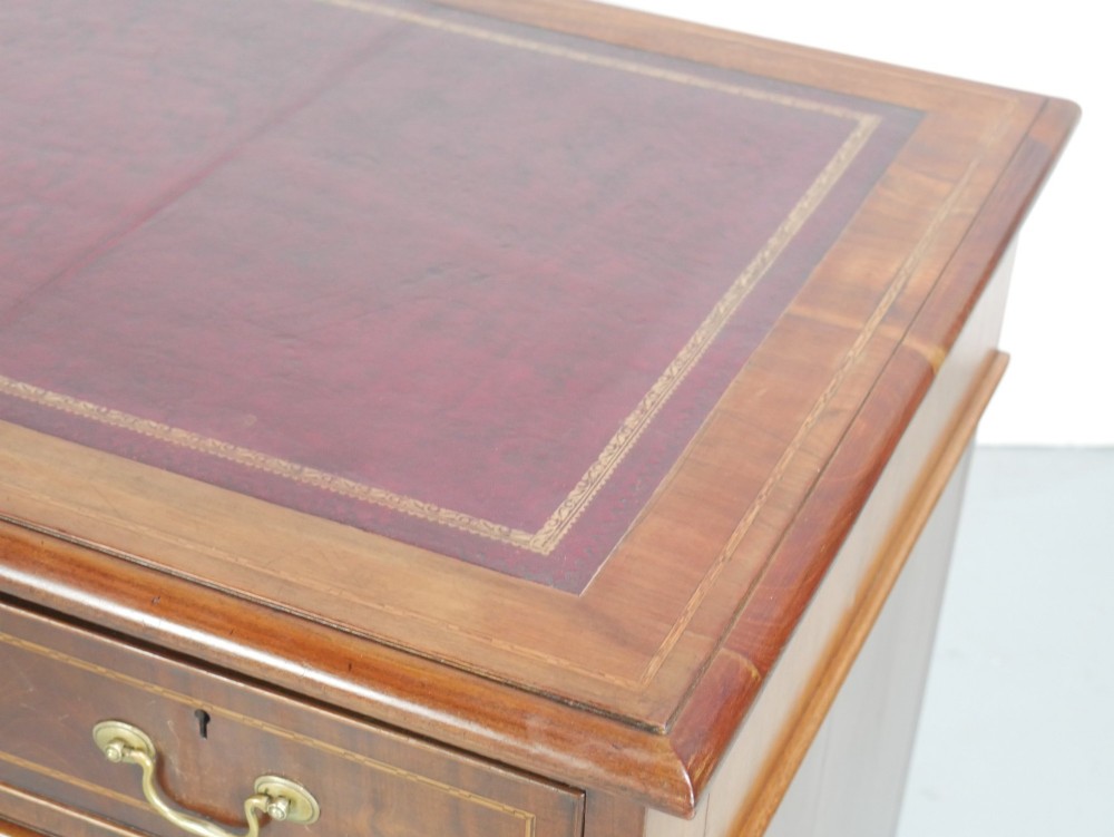 An Edwardian mahogany kneehole pedestal desk featuring an inset writing top, inlaid drawer borders, and nine drawers fitted with brass swan-neck handles. View IV