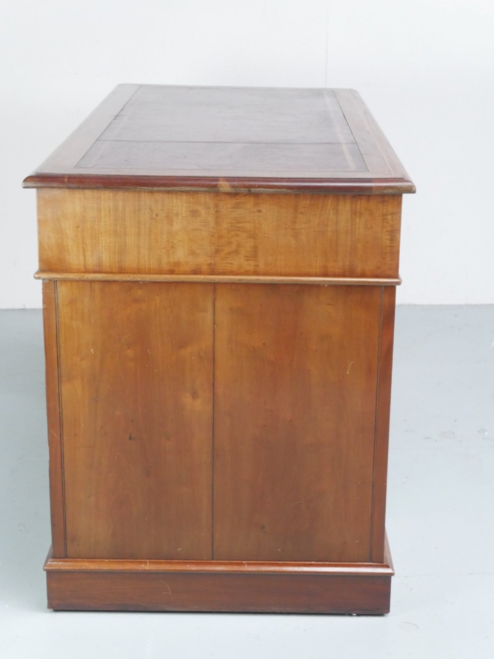 An Edwardian mahogany kneehole pedestal desk featuring an inset writing top, inlaid drawer borders, and nine drawers fitted with brass swan-neck handles. View V