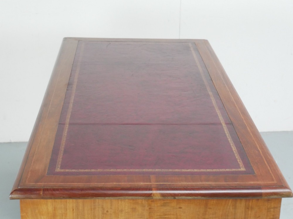 An Edwardian mahogany kneehole pedestal desk featuring an inset writing top, inlaid drawer borders, and nine drawers fitted with brass swan-neck handles. View VI