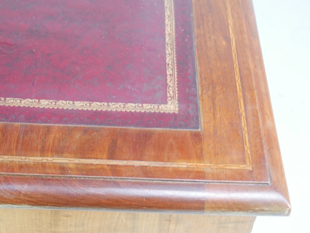 An Edwardian mahogany kneehole pedestal desk featuring an inset writing top, inlaid drawer borders, and nine drawers fitted with brass swan-neck handles. View VII