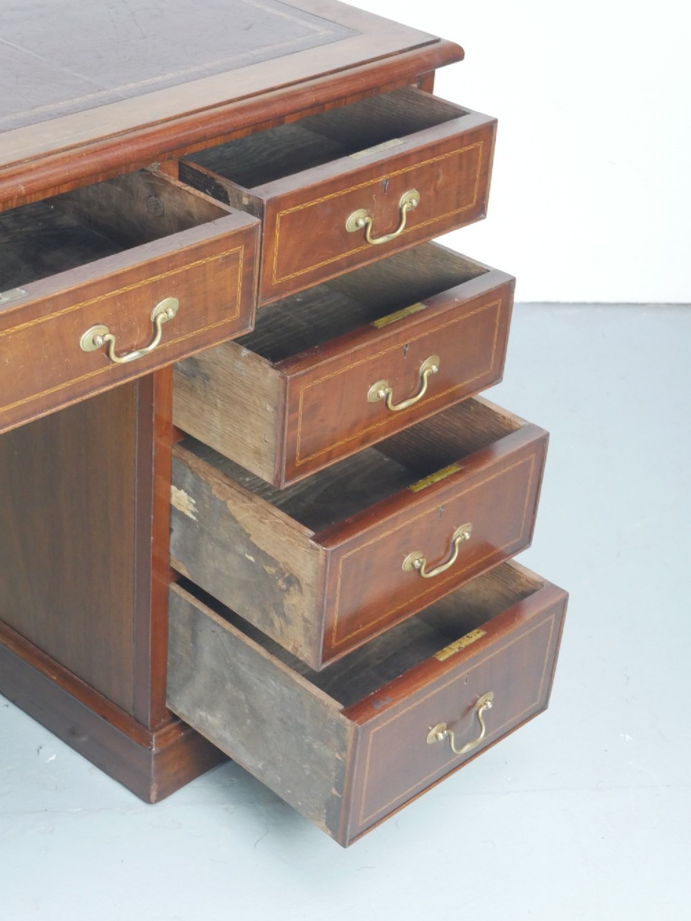 An Edwardian mahogany kneehole pedestal desk featuring an inset writing top, inlaid drawer borders, and nine drawers fitted with brass swan-neck handles. View X