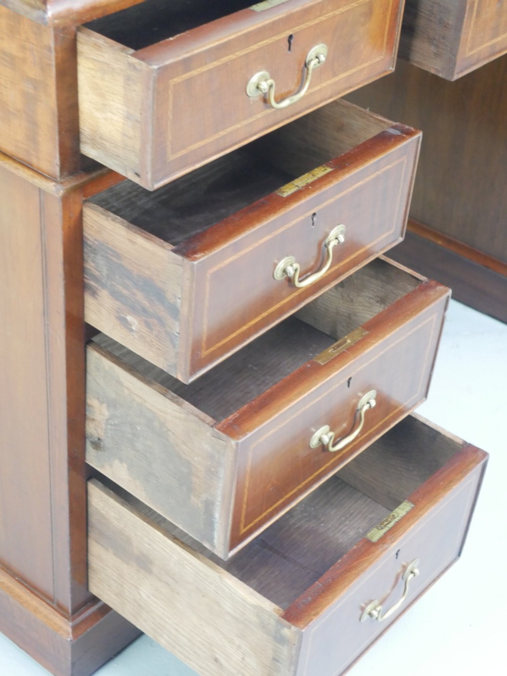 An Edwardian mahogany kneehole pedestal desk featuring an inset writing top, inlaid drawer borders, and nine drawers fitted with brass swan-neck handles. View XI