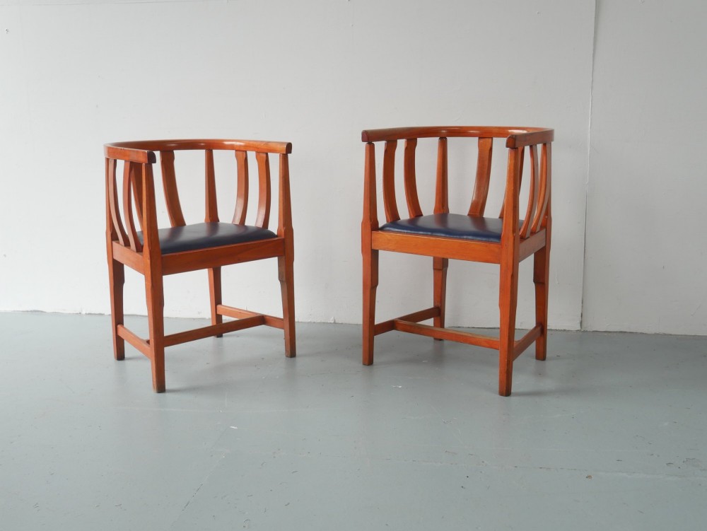 A pair of warm brown hardwood tub armchairs featuring curved slatted backrests and navy blue upholstered seats.