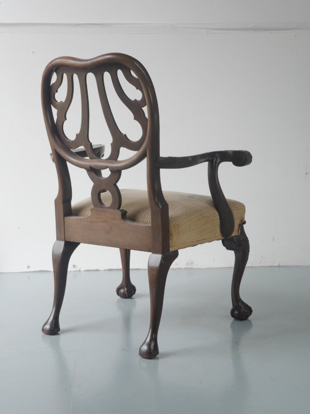 A carved mahogany armchair featuring an ornate pierced splat back, scrolled arms, tan striped fabric upholstery, and cabriole front legs with claw-and-ball feet. View II