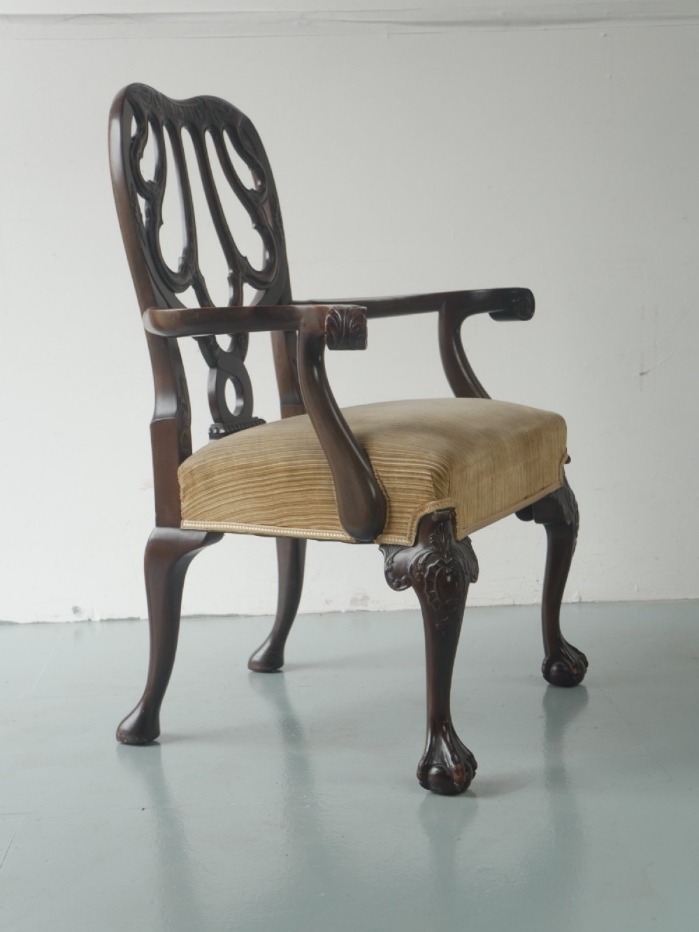 A carved mahogany armchair featuring an ornate pierced splat back, scrolled arms, tan striped fabric upholstery, and cabriole front legs with claw-and-ball feet. View III