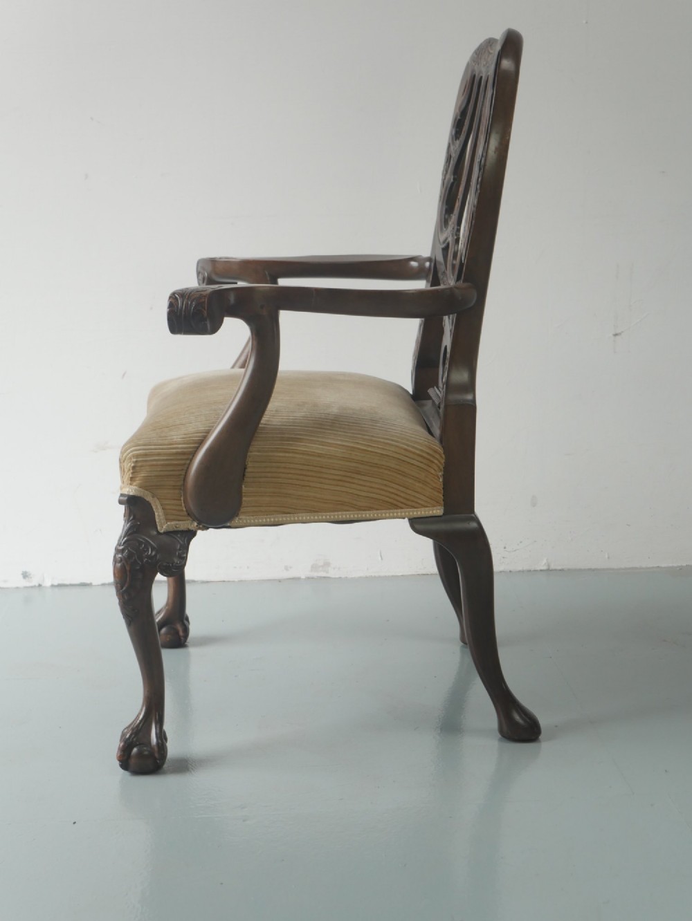 A carved mahogany armchair featuring an ornate pierced splat back, scrolled arms, tan striped fabric upholstery, and cabriole front legs with claw-and-ball feet. View IV