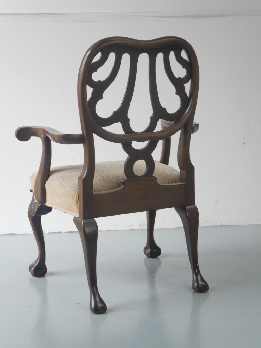 A carved mahogany armchair featuring an ornate pierced splat back, scrolled arms, tan striped fabric upholstery, and cabriole front legs with claw-and-ball feet. View V