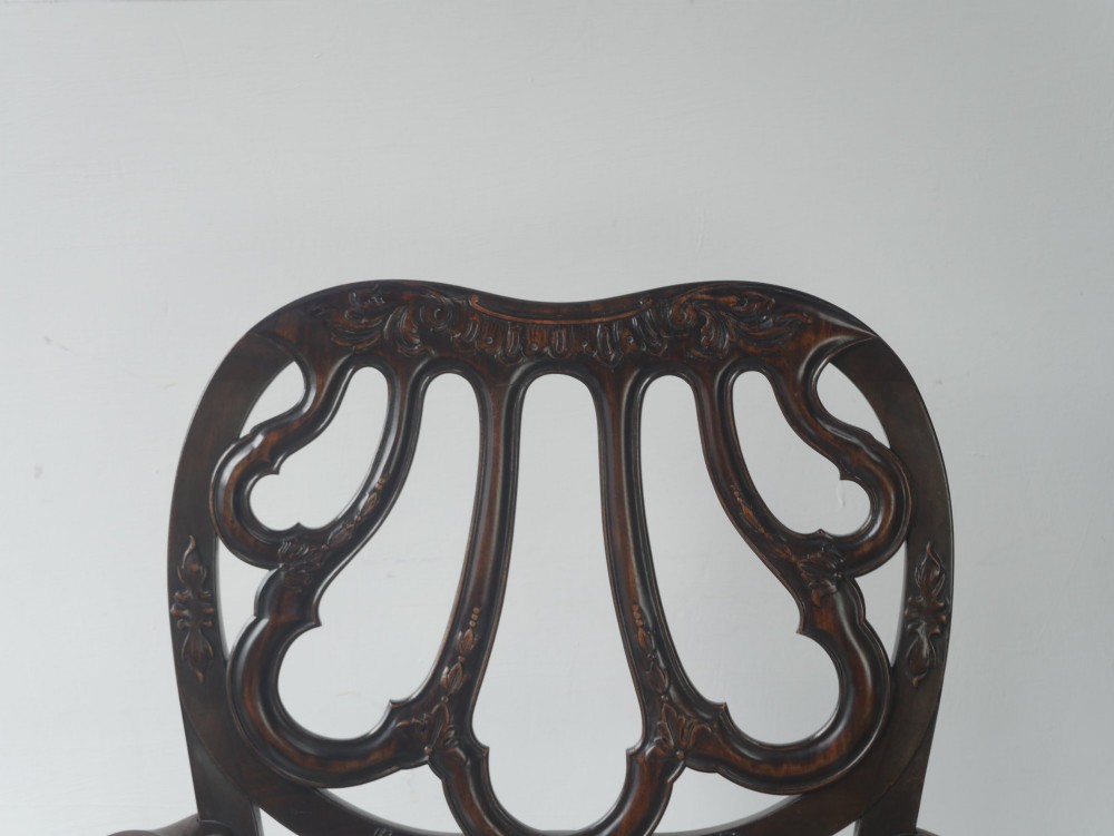 A carved mahogany armchair featuring an ornate pierced splat back, scrolled arms, tan striped fabric upholstery, and cabriole front legs with claw-and-ball feet. View X