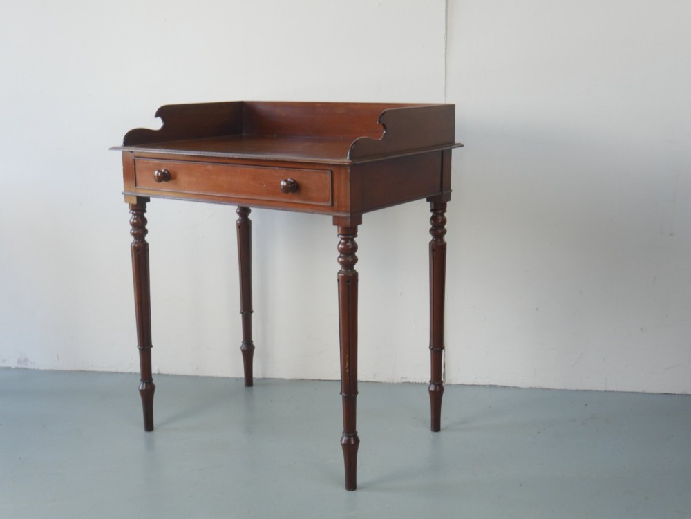 A 19th-century mahogany writing table featuring turned legs, a single frieze drawer with wooden knobs, and a raised gallery back.