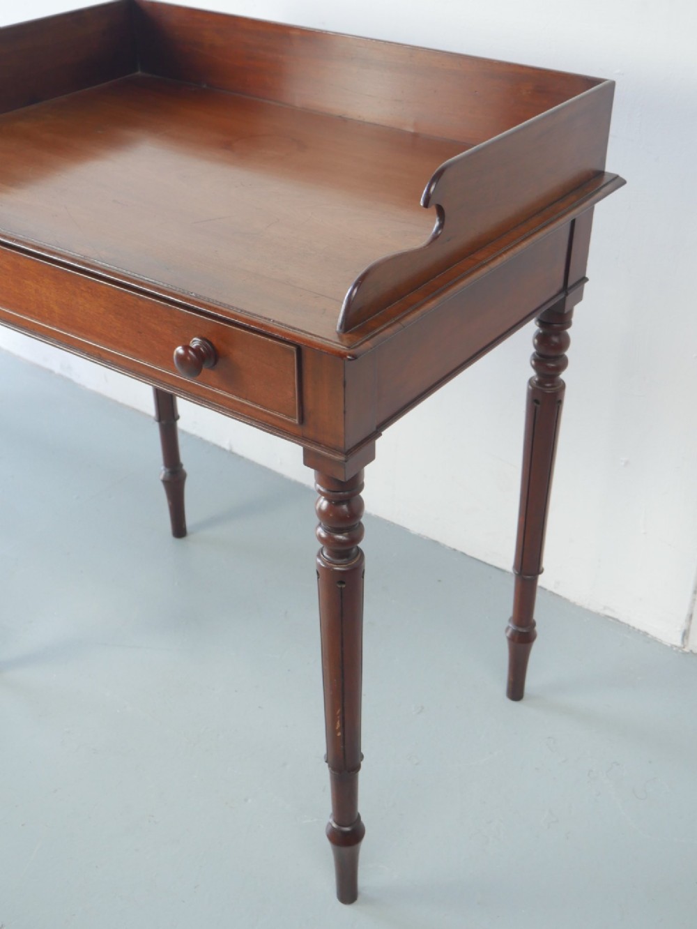 A 19th-century mahogany writing table featuring turned legs, a single frieze drawer with wooden knobs, and a raised gallery back. View V