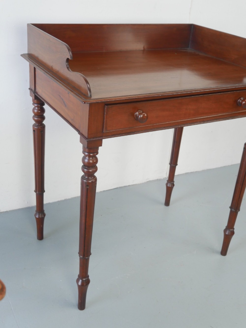 A 19th-century mahogany writing table featuring turned legs, a single frieze drawer with wooden knobs, and a raised gallery back. View VI