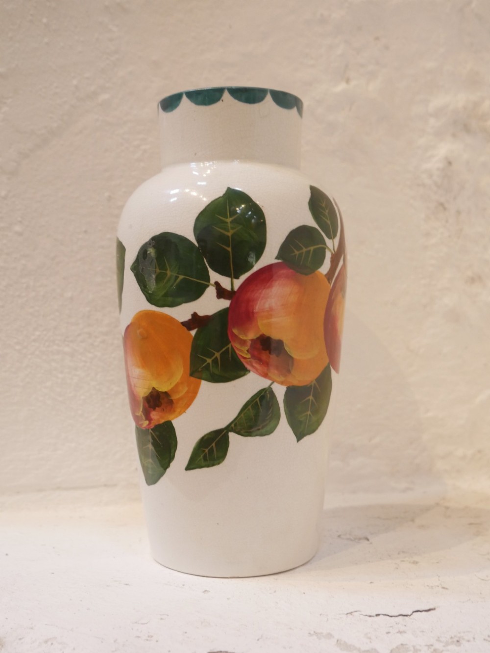 A cylindrical cream earthenware vase hand-painted with green leaves, yellow apples, and a green scalloped rim detail.