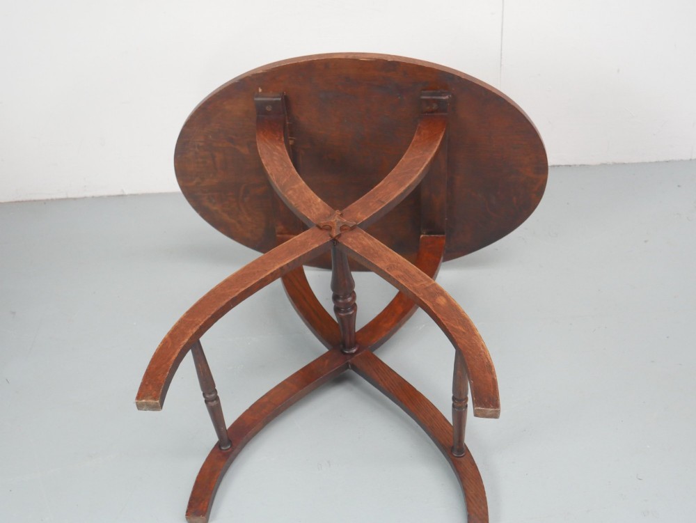 A circular oak lamp table featuring curved cross-framed legs joined by turned stretchers. View X