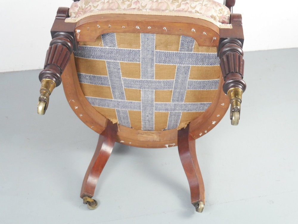 A Regency mahogany armchair with floral patterned fabric upholstery, scroll arms, reeded front legs, and brass castors. View IV