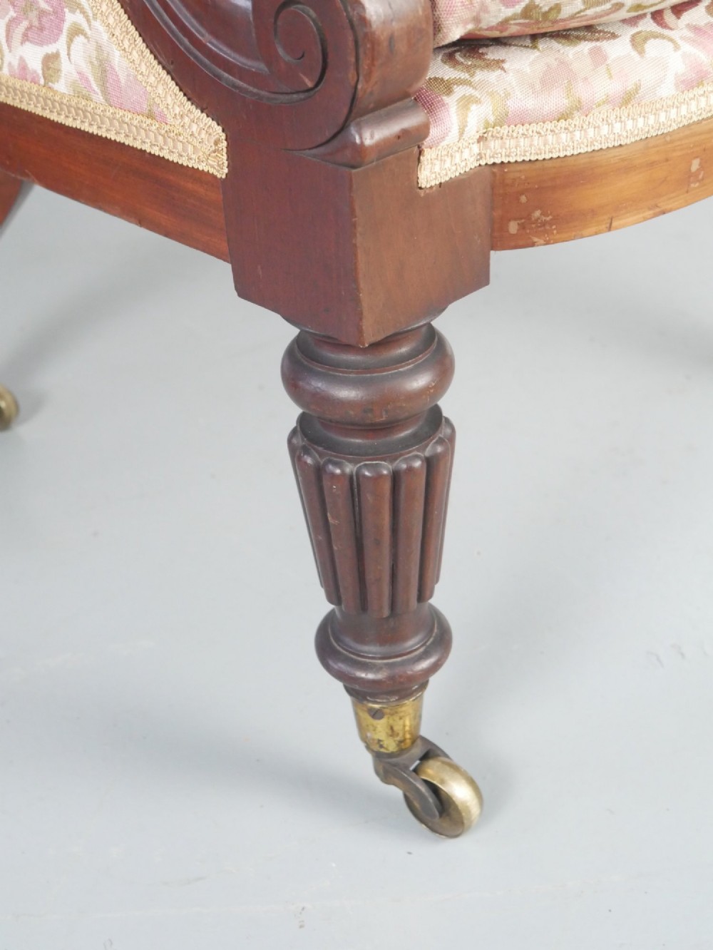 A Regency mahogany armchair with floral patterned fabric upholstery, scroll arms, reeded front legs, and brass castors. View V