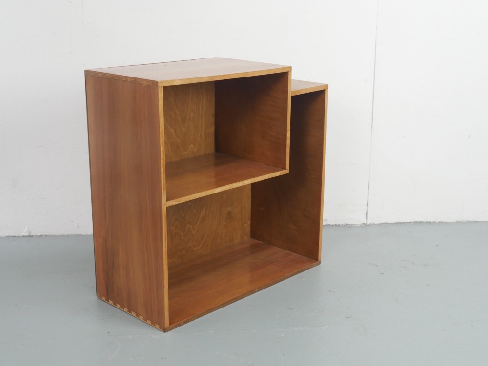 A mid-century open wooden side cabinet featuring asymmetrical shelving compartments and visible comb joints at the outer edges.
