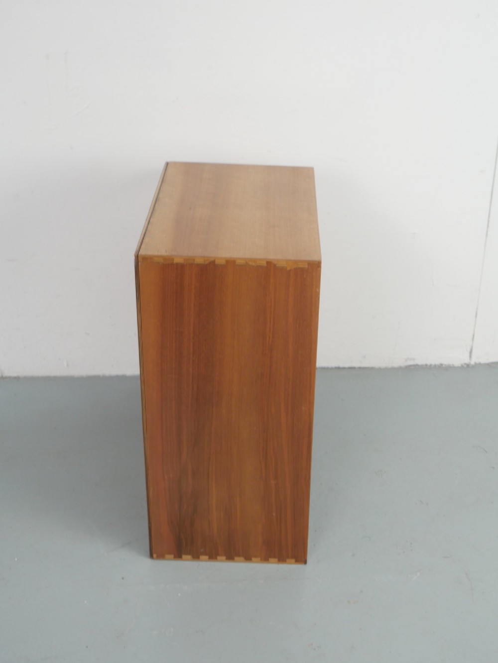 A mid-century open wooden side cabinet featuring asymmetrical shelving compartments and visible comb joints at the outer edges. View III