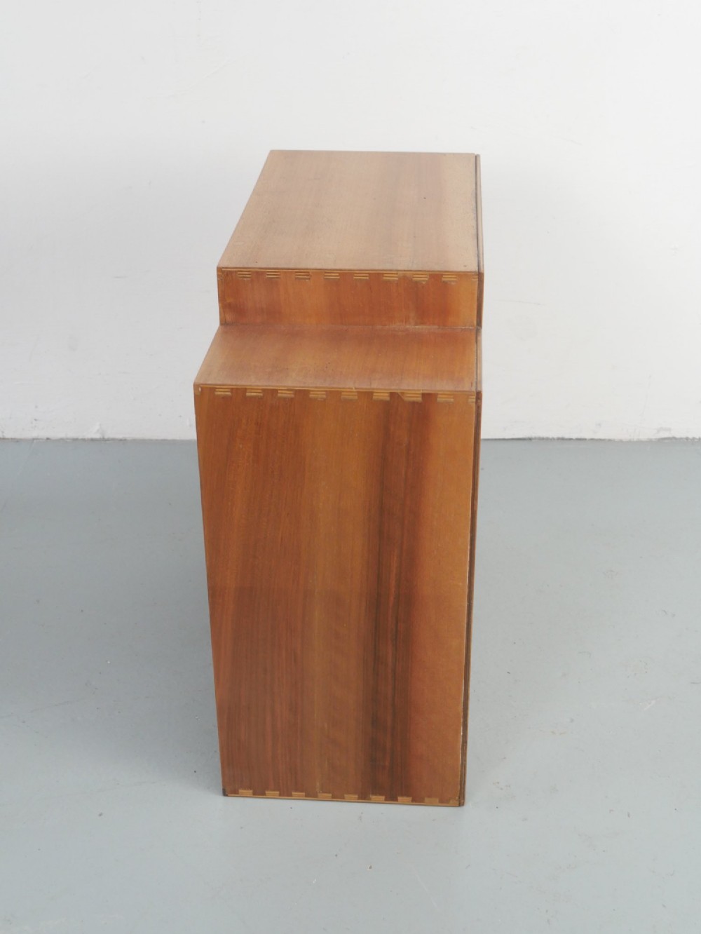 A mid-century open wooden side cabinet featuring asymmetrical shelving compartments and visible comb joints at the outer edges. View V