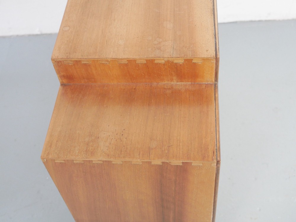 A mid-century open wooden side cabinet featuring asymmetrical shelving compartments and visible comb joints at the outer edges. View VI