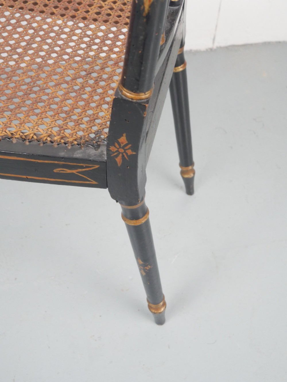 A black painted and parcel-gilt antique Sheraton window seat featuring pointed arch end splats and a floral needlepoint cushion. View IV