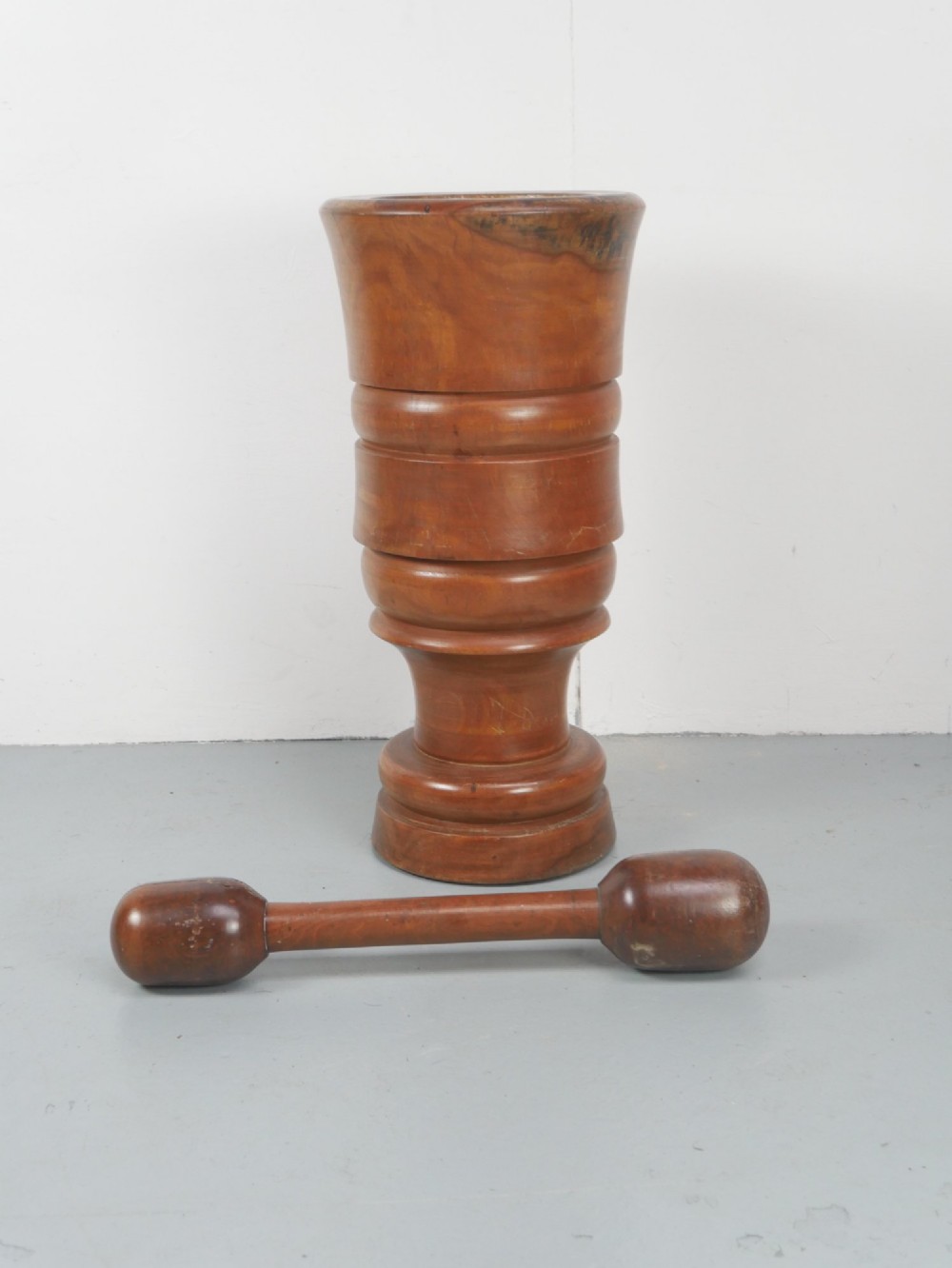 A large turned wooden mortar with ribbed bands on its exterior and a matching pestle resting inside. View II