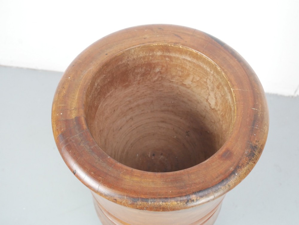 A large turned wooden mortar with ribbed bands on its exterior and a matching pestle resting inside. View III