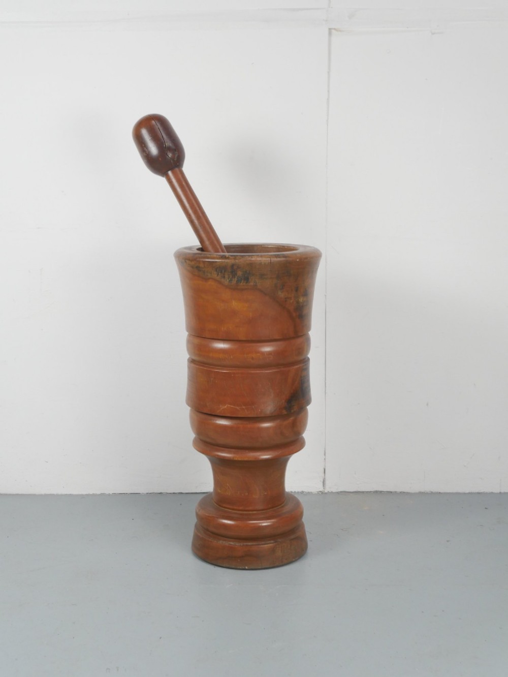 A large turned wooden mortar with ribbed bands on its exterior and a matching pestle resting inside. View VII
