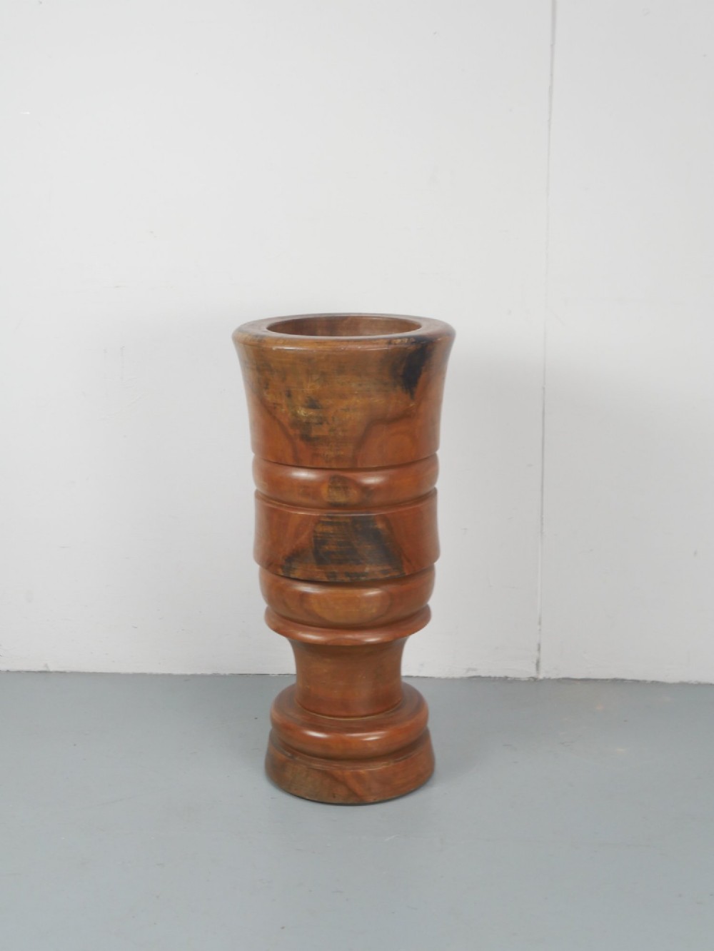 A large turned wooden mortar with ribbed bands on its exterior and a matching pestle resting inside. View VIII